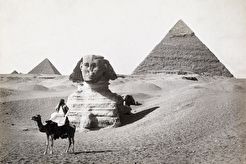 A man poses on a camel in front of the Great Sphinx and the pyramids of Giza (1913)